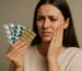Mujer con dolor de muelas sosteniendo blísteres de medicamentos