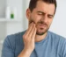 Persona joven con dolor de mandíbula tocándose la cara en casa, imagen realista y luminosa que representa tensión mandibular o bruxismo.
